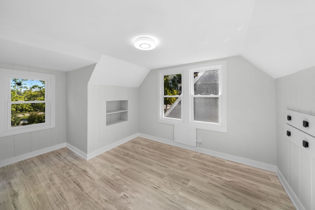 bonus room featuring light wood-type flooring, built in features, and lofted ceiling