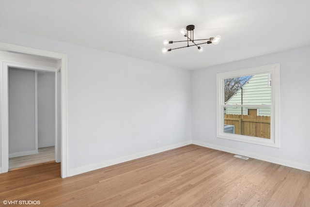 empty room with light wood-type flooring and a notable chandelier