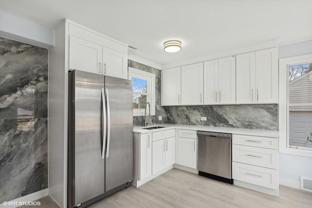 kitchen with appliances with stainless steel finishes, light wood-type flooring, tasteful backsplash, sink, and white cabinetry