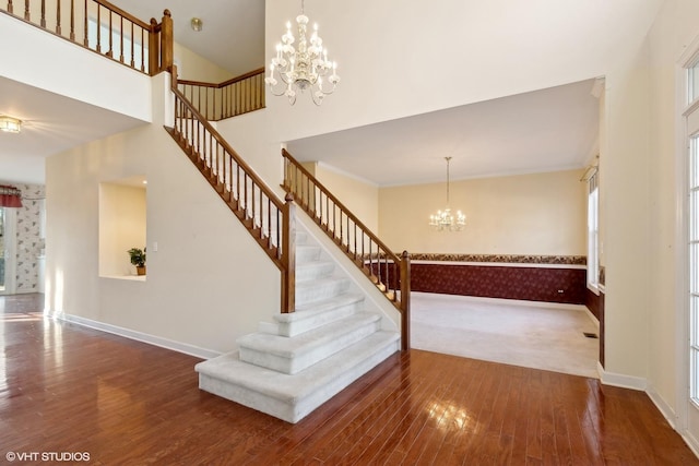 stairway with a towering ceiling, wood-type flooring, ornamental molding, and a chandelier