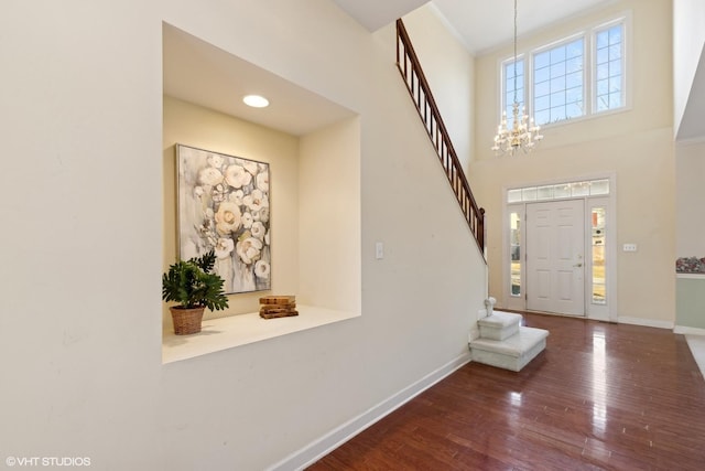 entryway with a towering ceiling, a notable chandelier, and dark hardwood / wood-style flooring