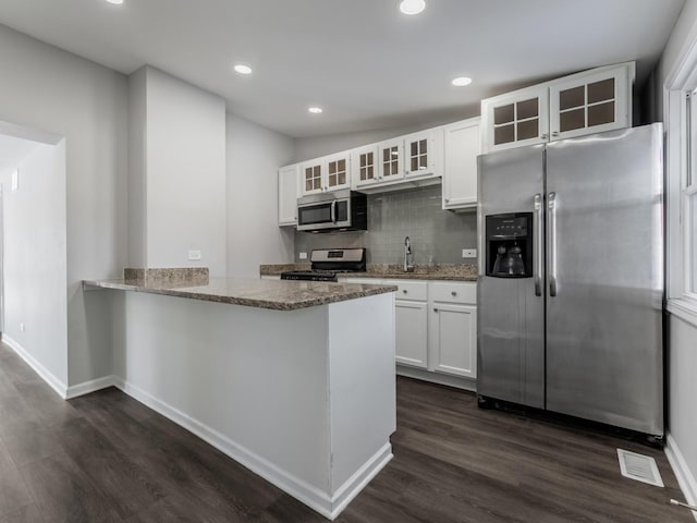 kitchen with stone counters, white cabinets, appliances with stainless steel finishes, dark hardwood / wood-style flooring, and kitchen peninsula