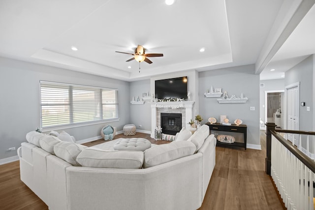 living room with ceiling fan, a stone fireplace, dark hardwood / wood-style flooring, and a tray ceiling