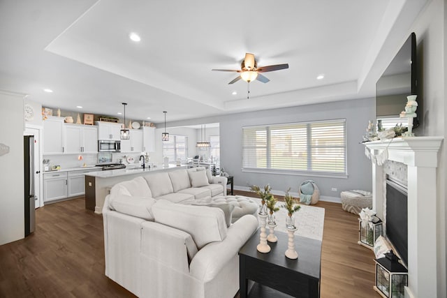 living room featuring ceiling fan, dark wood-type flooring, sink, and a raised ceiling