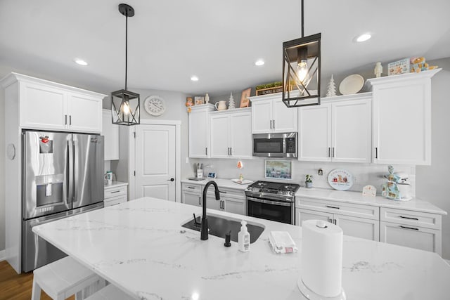 kitchen with decorative light fixtures, sink, appliances with stainless steel finishes, and an island with sink