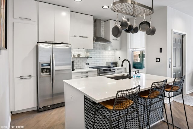 kitchen with a center island with sink, white cabinets, wall chimney exhaust hood, appliances with stainless steel finishes, and a kitchen bar