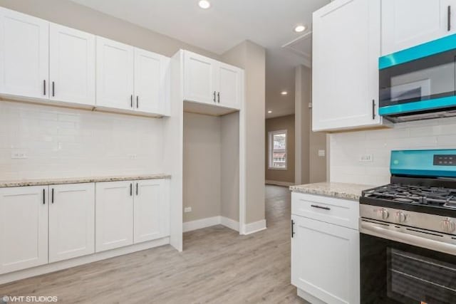 kitchen with white cabinets, light stone counters, appliances with stainless steel finishes, and light hardwood / wood-style flooring