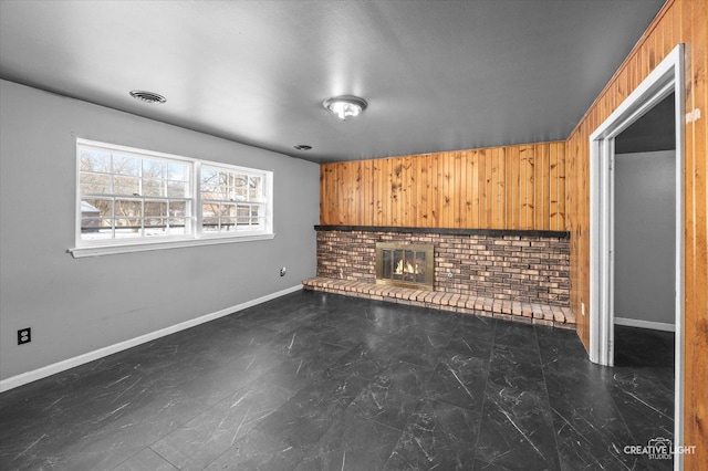 unfurnished living room featuring a brick fireplace and wooden walls