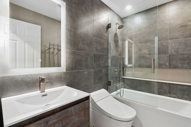 full bathroom with tile walls, shower / bath combination with glass door, vanity, and toilet