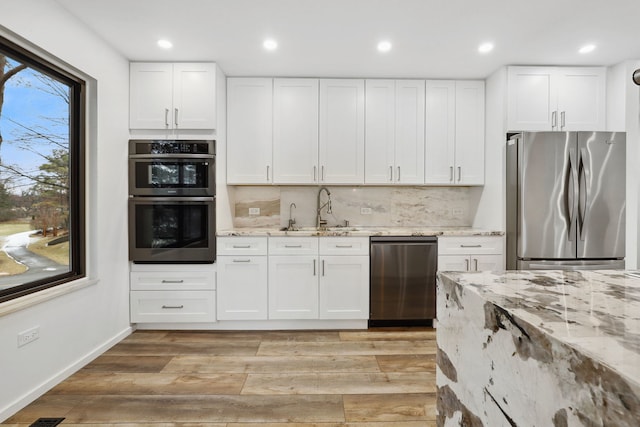 kitchen with sink, light stone counters, white cabinets, and stainless steel appliances