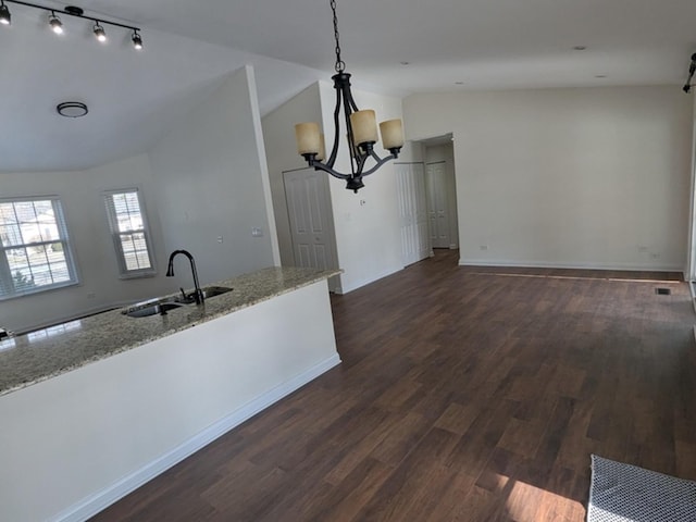 kitchen featuring vaulted ceiling, light stone counters, sink, and decorative light fixtures