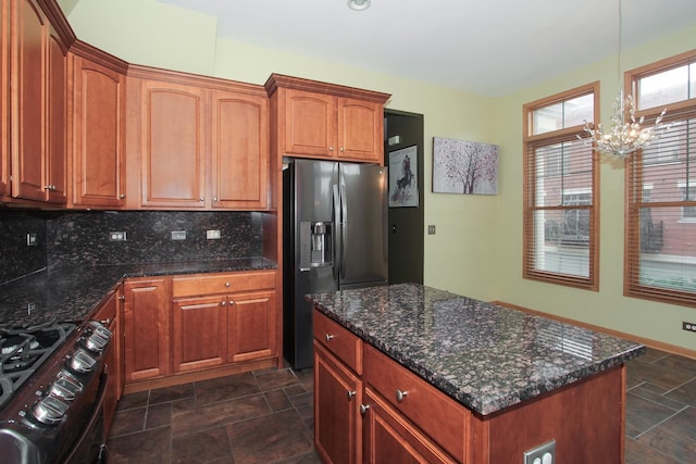 kitchen with backsplash, dark stone counters, black stove, stainless steel fridge, and a notable chandelier