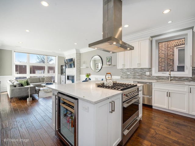 kitchen with beverage cooler, stainless steel appliances, white cabinets, open floor plan, and island exhaust hood