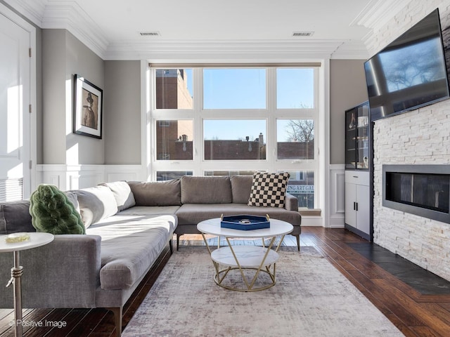 living room featuring wainscoting, ornamental molding, dark wood-style flooring, and a stone fireplace