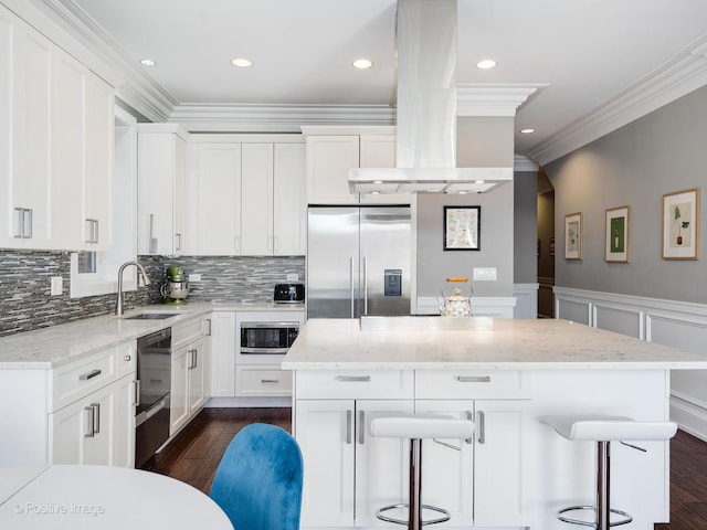 kitchen with a breakfast bar, white cabinetry, island range hood, and built in appliances