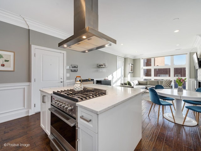 kitchen with island range hood, ornamental molding, open floor plan, stainless steel stove, and white cabinetry