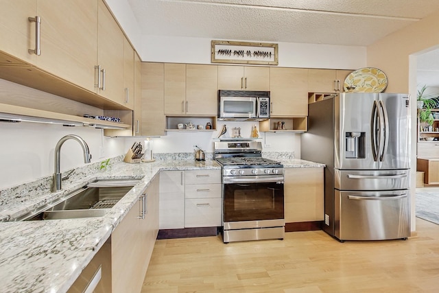 kitchen with sink, light wood-type flooring, appliances with stainless steel finishes, a textured ceiling, and light stone counters