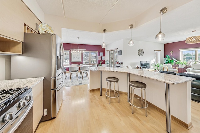 kitchen featuring decorative light fixtures, light wood-type flooring, stainless steel gas range, and a breakfast bar area