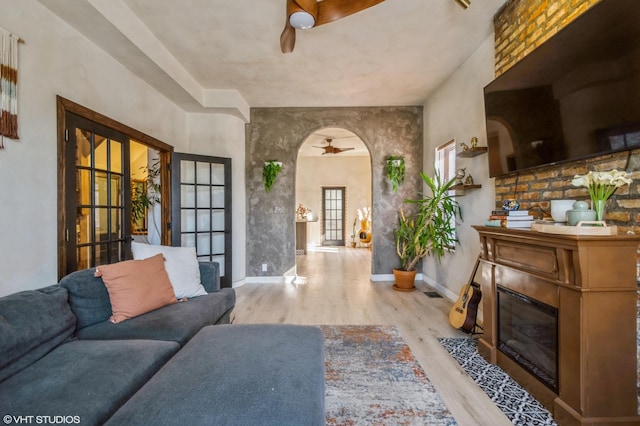 living area with arched walkways, a fireplace with flush hearth, wood finished floors, a ceiling fan, and baseboards