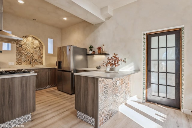 kitchen featuring light wood finished floors, stainless steel fridge with ice dispenser, a peninsula, light countertops, and open shelves