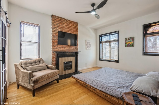 bedroom with light wood-type flooring, a fireplace, baseboards, and ceiling fan