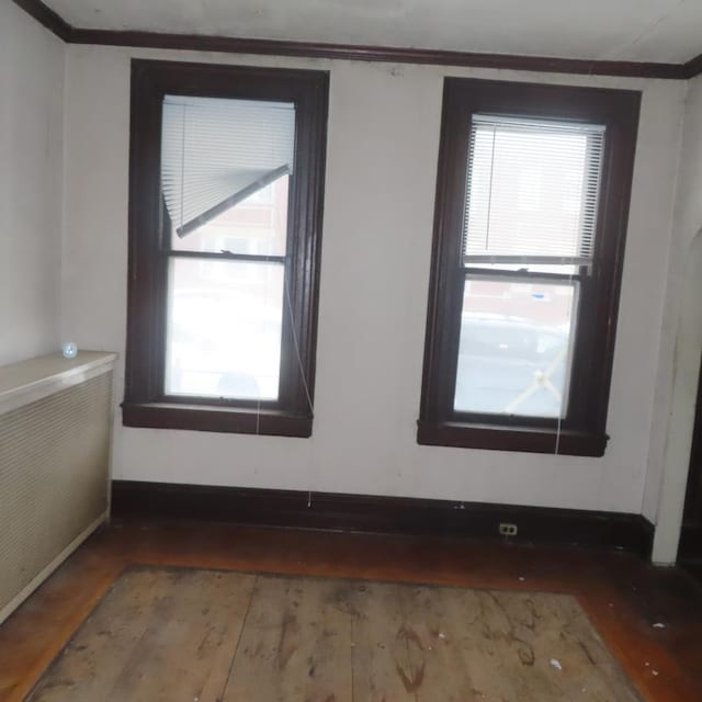 spare room featuring wood-type flooring, crown molding, and radiator