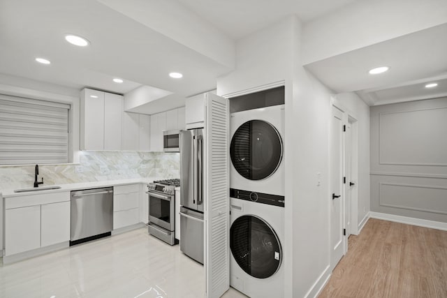 clothes washing area featuring stacked washer / drying machine, light hardwood / wood-style floors, and sink