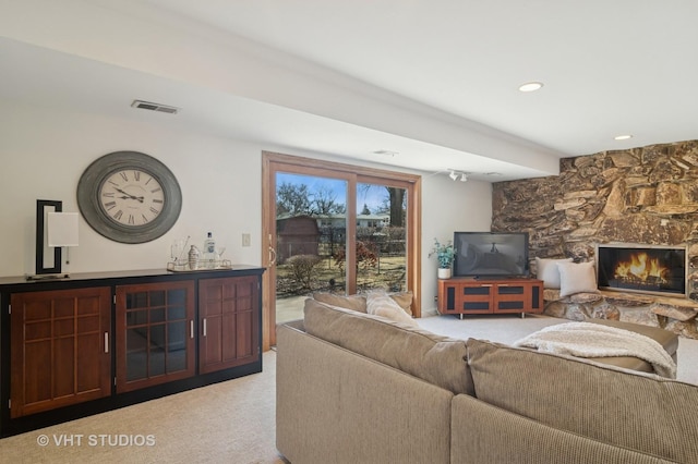 living area with visible vents, light colored carpet, and a stone fireplace