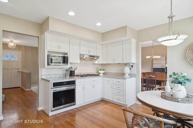 kitchen featuring under cabinet range hood, light wood-style flooring, stainless steel appliances, and light stone counters