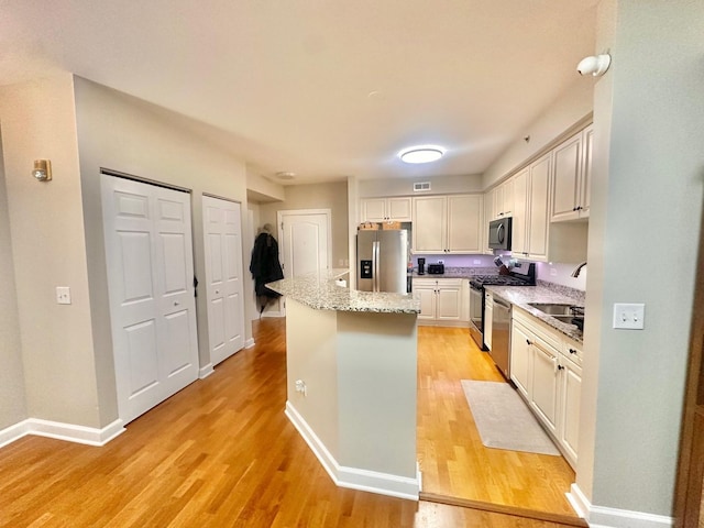 kitchen featuring light stone counters, a kitchen island, light wood-type flooring, appliances with stainless steel finishes, and sink