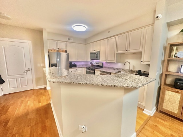 kitchen featuring stainless steel appliances, sink, white cabinets, light stone counters, and light wood-type flooring