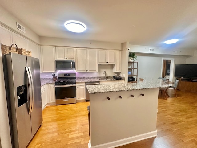 kitchen with sink, white cabinets, a center island, light wood-type flooring, and appliances with stainless steel finishes