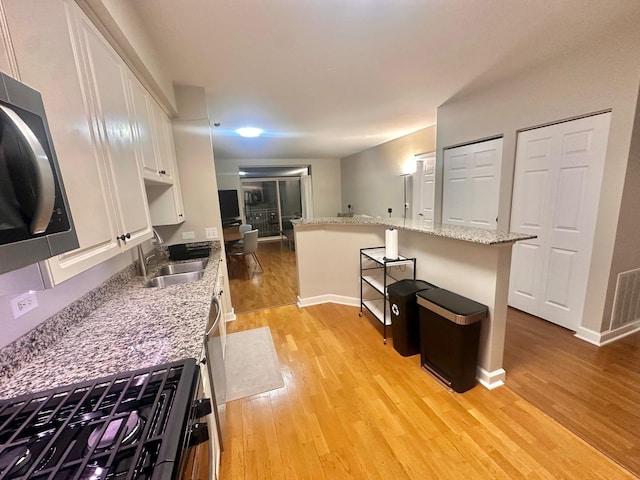 kitchen featuring light stone counters, light hardwood / wood-style floors, a breakfast bar, white cabinetry, and sink