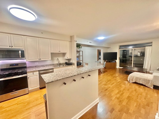 kitchen with stainless steel appliances, white cabinetry, light hardwood / wood-style flooring, and light stone countertops