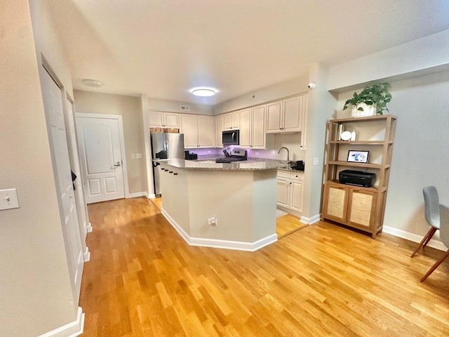 kitchen featuring appliances with stainless steel finishes, light hardwood / wood-style flooring, white cabinetry, and light stone counters