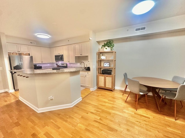 kitchen with stainless steel appliances, a center island, white cabinetry, light stone counters, and light hardwood / wood-style floors