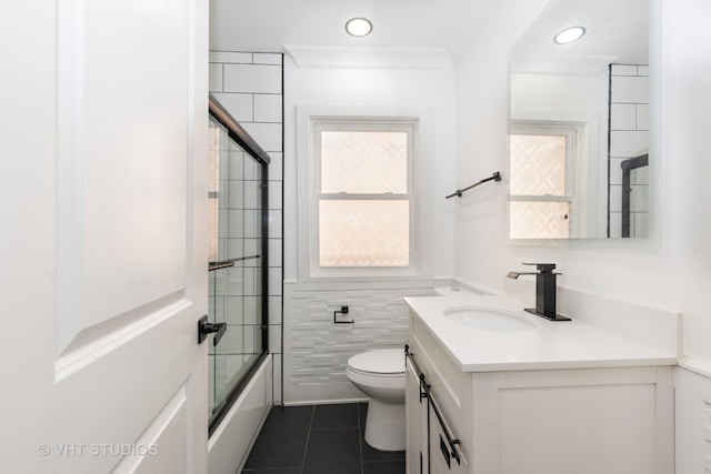 full bathroom with tile patterned flooring, toilet, shower / bath combination with glass door, vanity, and tile walls