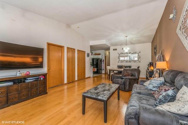 living room featuring an inviting chandelier, light hardwood / wood-style flooring, and vaulted ceiling