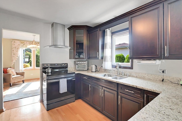 kitchen with light stone counters, sink, wall chimney range hood, light hardwood / wood-style flooring, and stainless steel range with electric cooktop