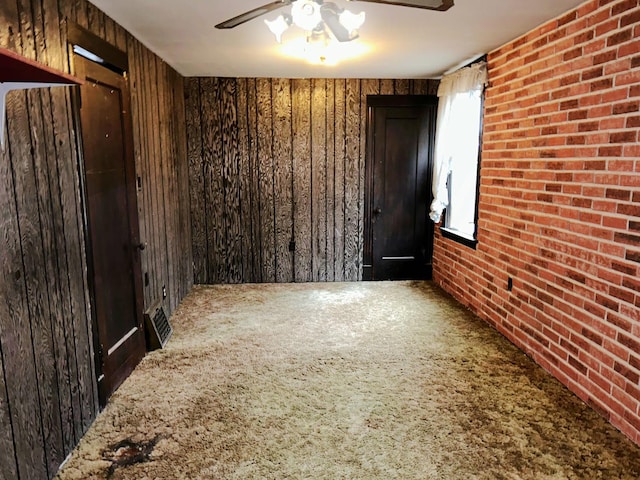 empty room featuring carpet, brick wall, ceiling fan, and wood walls