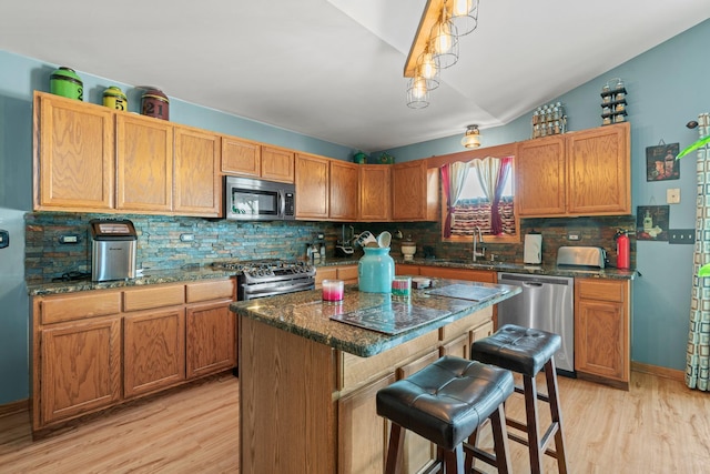 kitchen with stainless steel appliances, sink, lofted ceiling, light wood-type flooring, and a kitchen island