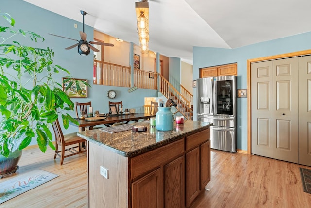 kitchen featuring ceiling fan, light hardwood / wood-style floors, dark stone counters, stainless steel fridge with ice dispenser, and a kitchen island