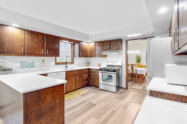 kitchen featuring white appliances, sink, light stone countertops, light wood-type flooring, and kitchen peninsula