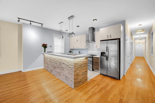 kitchen featuring pendant lighting, wall chimney range hood, stainless steel appliances, tasteful backsplash, and light wood-type flooring