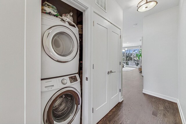 washroom with stacked washer and dryer and dark wood-type flooring