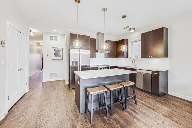 kitchen with wall chimney exhaust hood, a center island, decorative light fixtures, a kitchen bar, and appliances with stainless steel finishes