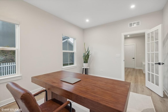 office with a wealth of natural light, light hardwood / wood-style floors, and french doors