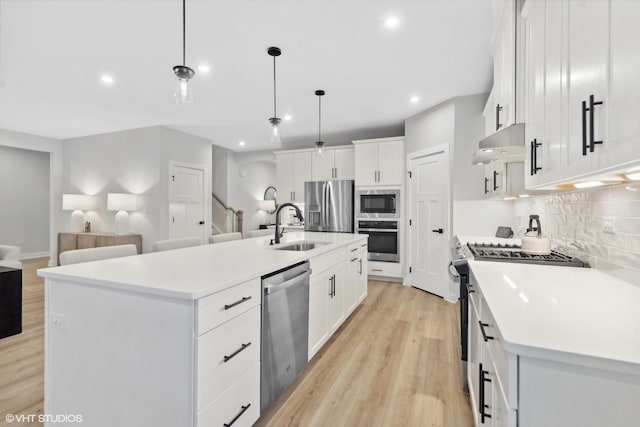 kitchen with pendant lighting, white cabinetry, sink, stainless steel appliances, and a center island with sink