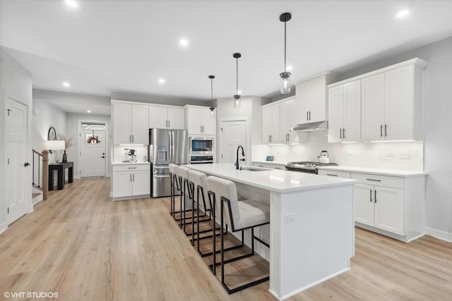 kitchen featuring white cabinetry, appliances with stainless steel finishes, decorative light fixtures, and an island with sink