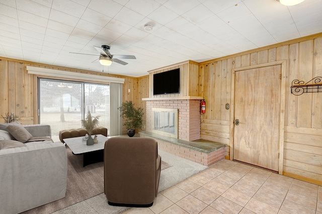 tiled living room with ceiling fan, a fireplace, and wooden walls